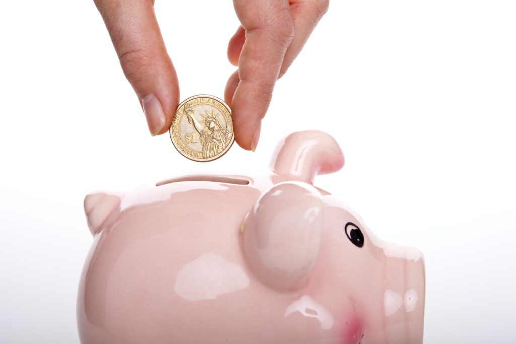 A savings piggy bank with a hand dropping a gold coin into it to symbolise personal finance